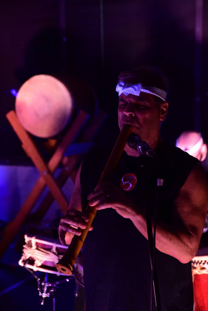 Musician playing the didgeridoo at night, surrounded by drums, enhancing the rhythmic and healing experience.